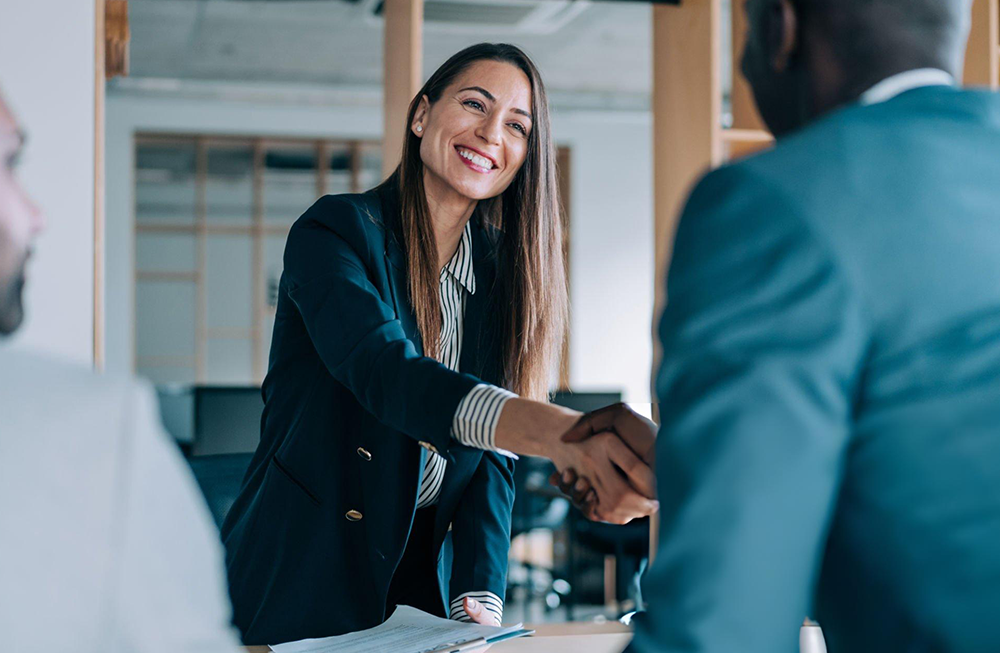 woman in a suit smiling and shaking a man's hand