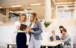 two women standing in a bright room looking at a tablet