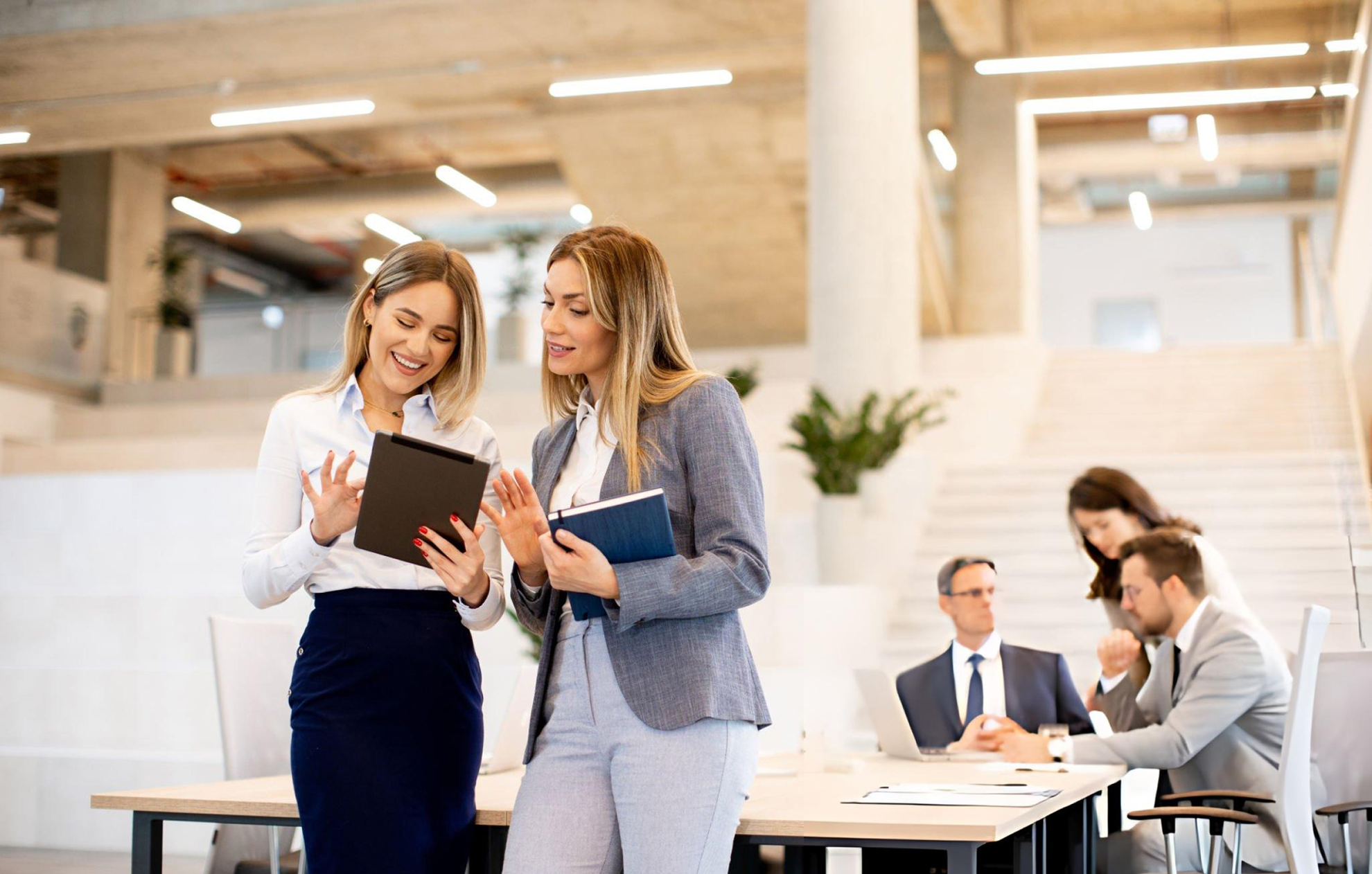 two women standing in a bright room looking at a tablet