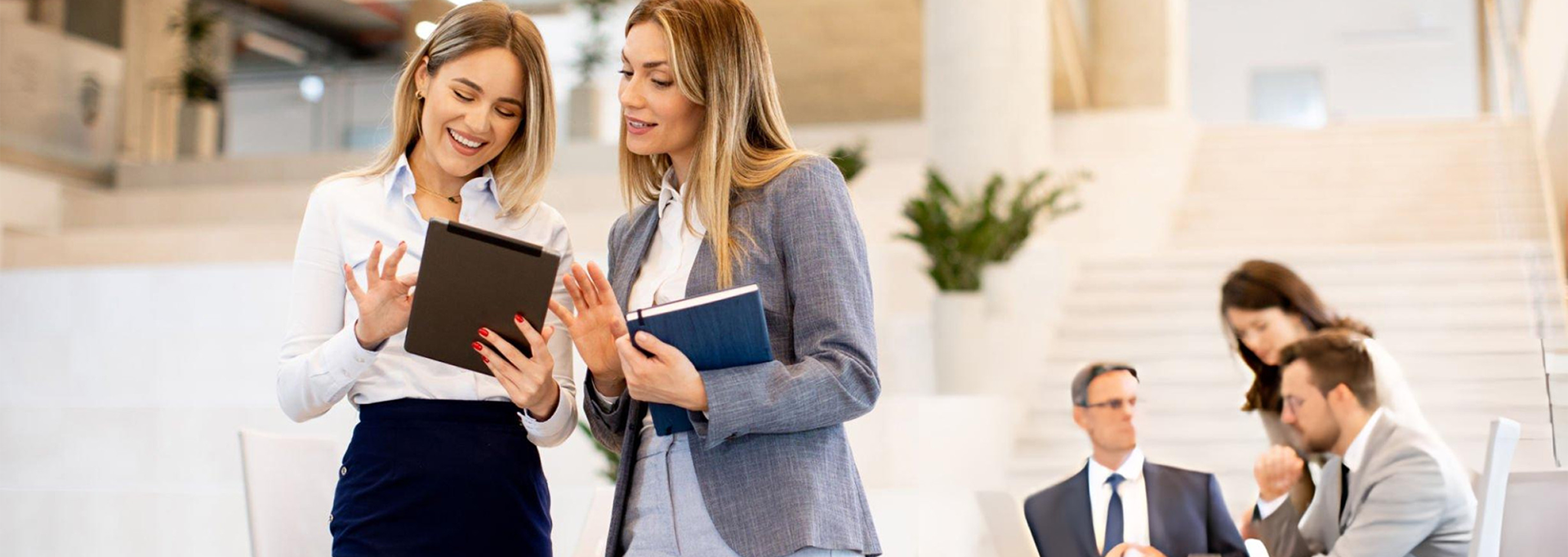 two women standing in a bright room looking at a tablet